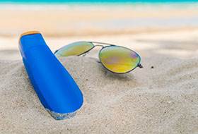 Sunglasses and sun cream on white  sand beach